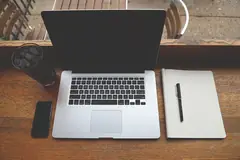 Лаптоп, телефон и тетрадка на дървено бюро